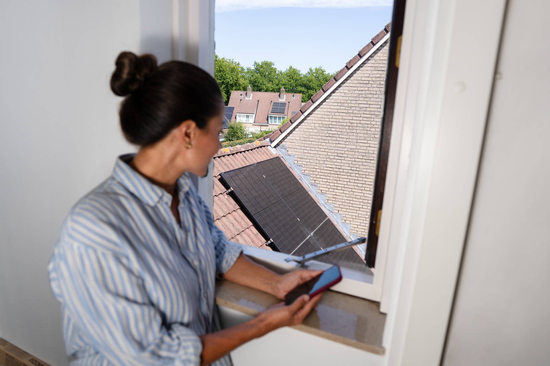 Vrouw kijk uit raam naar zonnepanelen op dak